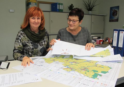 Ramona Müller und Ina Stimpel breiten den neuen Flächennutzungsplan der Gemeinde aus. Gut zu erkennen ist die angebrachte Siegelschnur der obersten Landesbehörde. Foto: Sebastian Pötzsch